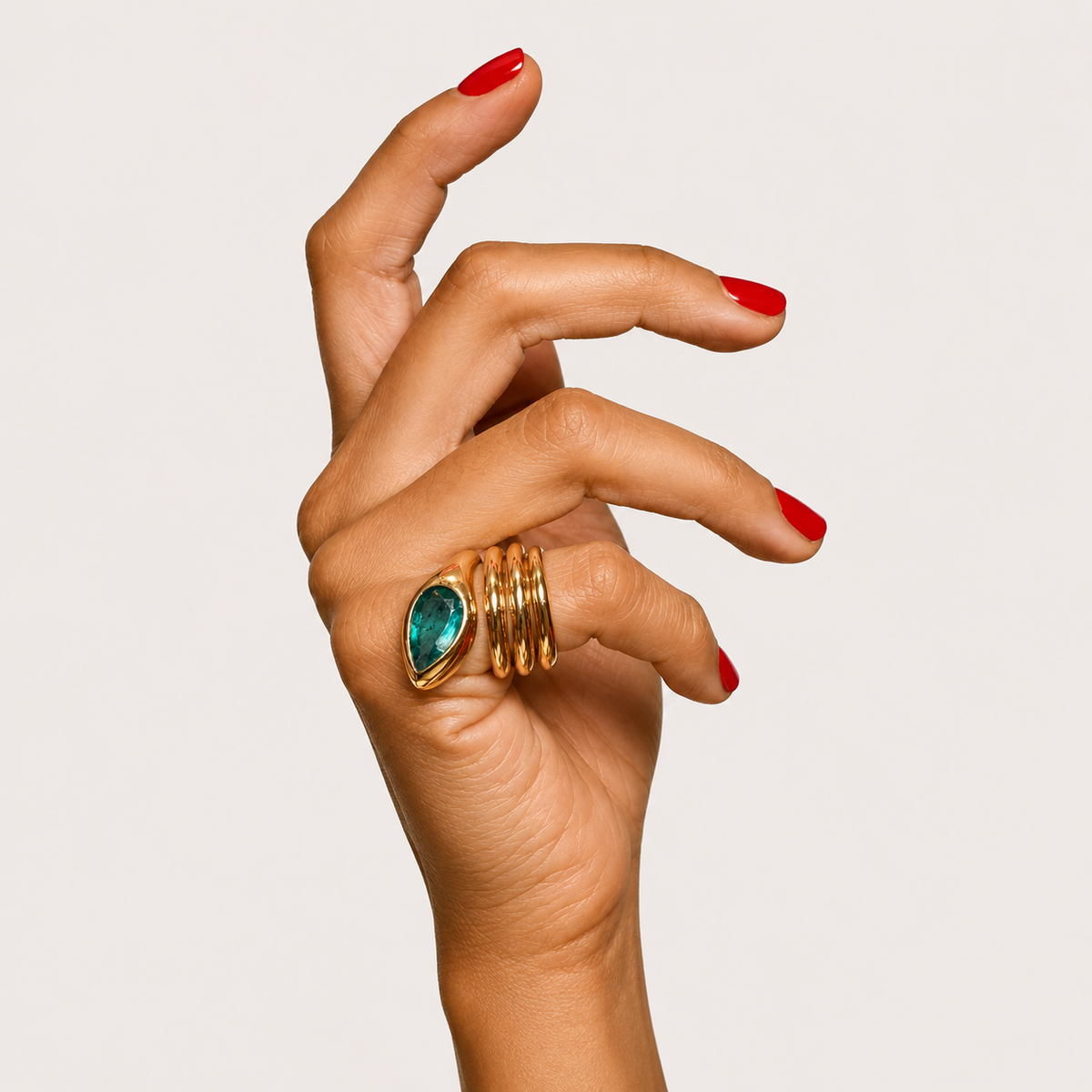 Sylvie 18K gold snake ring worn on a hand, showing three coils and a pear-shaped emerald head.
