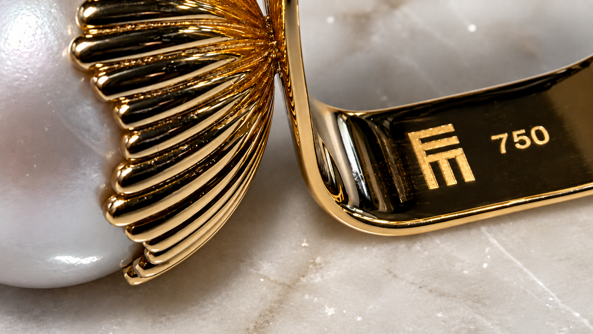 Close-up of a pearl ring’s fluted gold setting and inner band, engraved with the Elisabeth Marques monogram and 750 gold hallmark.