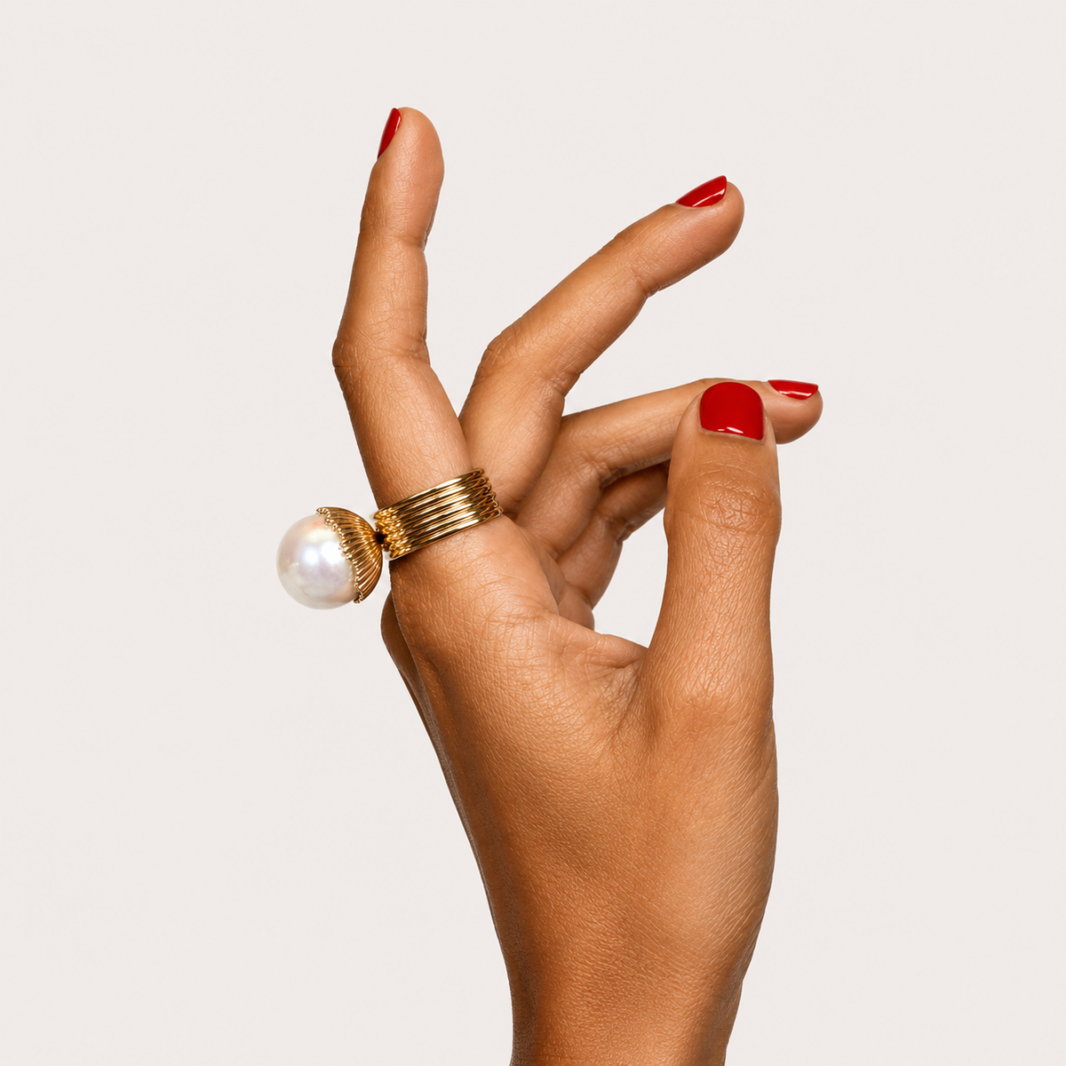 Loulou ring worn on a hand, showing a large white pearl raised above a wide gold band.