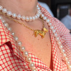 Gatsby gold dachshund necklace layered with pearl necklaces over a red-and-white gingham shirt.