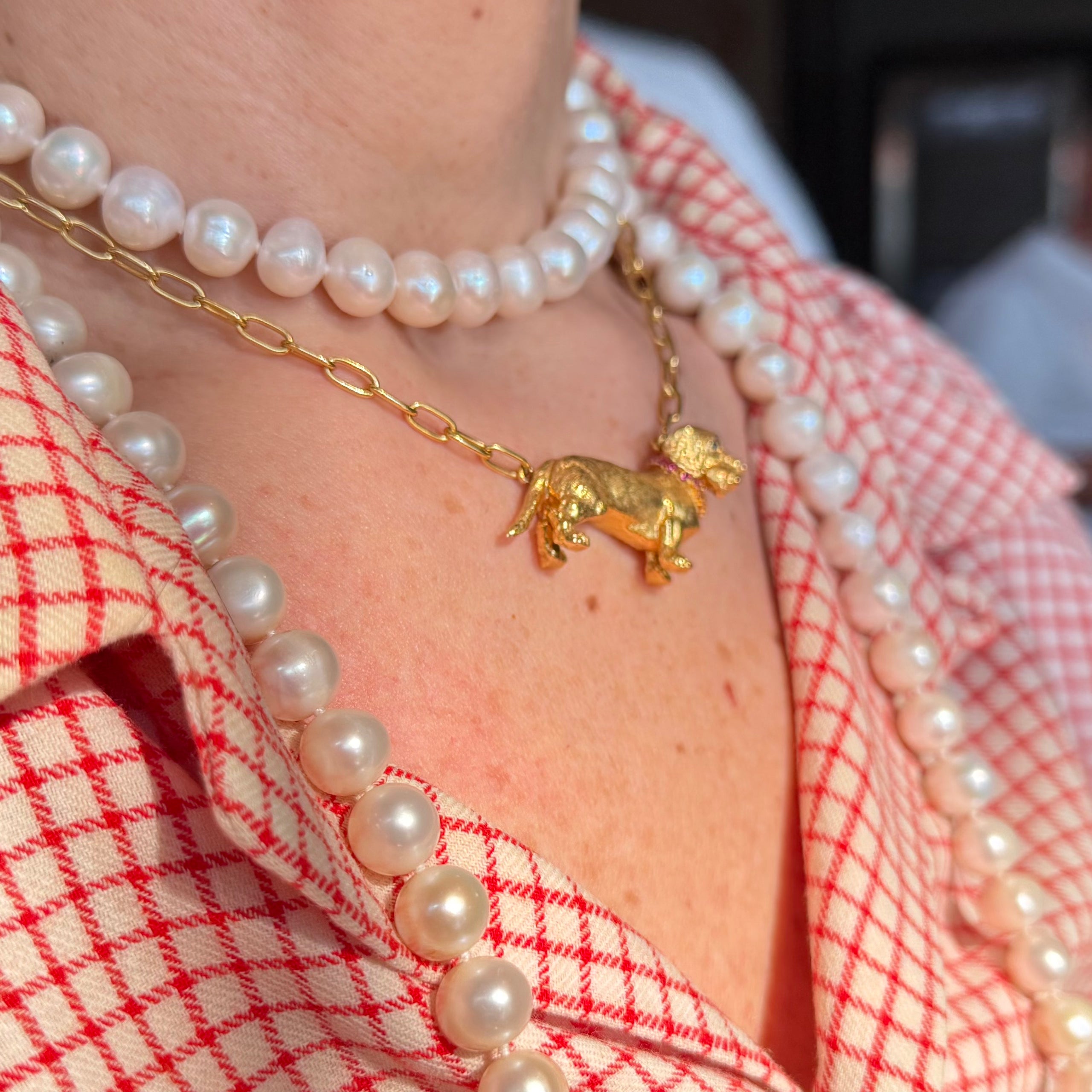 Gatsby gold dachshund necklace layered with pearl necklaces over a red-and-white gingham shirt.