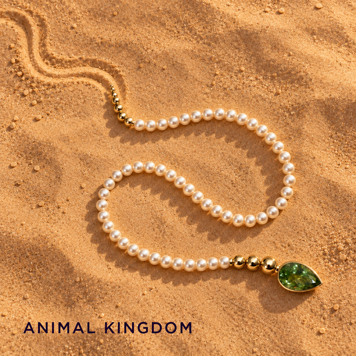 Salwa pearl and gold necklace arranged like a snake on sand, with a pear-shaped green peridot head — Animal Kingdom collection