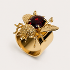 Angled view of the Buzz bumblebee ring, with a deep red gemstone body, textured gold head, engraved wings and a wide 18K gold band.