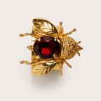 Top view of the Buzz bumblebee ring, showing its faceted red gemstone, engraved gold wings, textured head and six sculpted legs.
