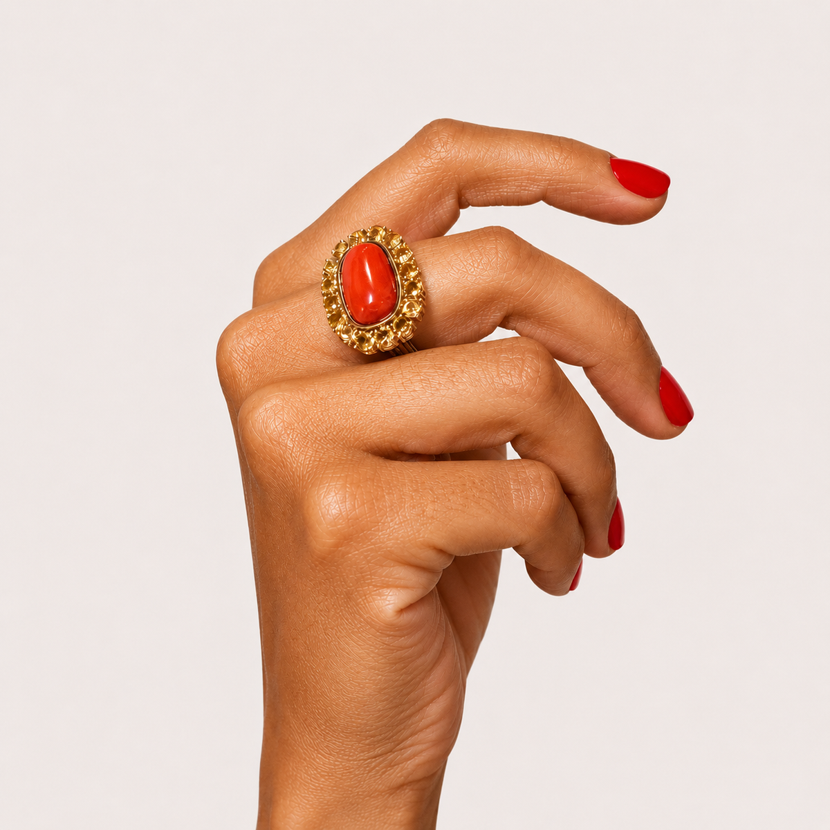Coralie 18K gold ring worn on a hand, with an oval red coral cabochon surrounded by golden sapphires.