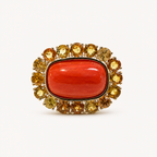 Front view of the Coralie 18K gold ring, with a smooth red Italian coral cabochon framed by round golden sapphires.