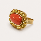 Angled view of the Coralie ring, showing its red Italian coral cabochon, golden sapphire halo and fluted 18K gold shoulders.