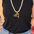 Gold Deco initial A pendant on a freshwater pearl necklace, worn over a black sleeveless top.