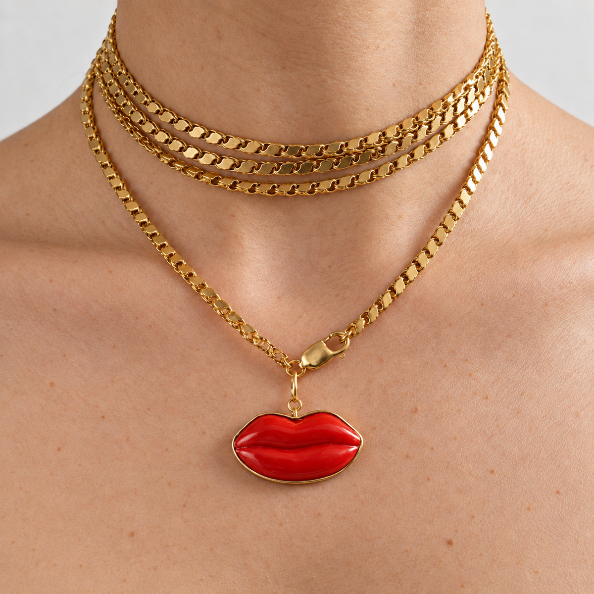 Dina red coral lips pendant framed in 18K gold, worn on a gold chain layered around the neck.