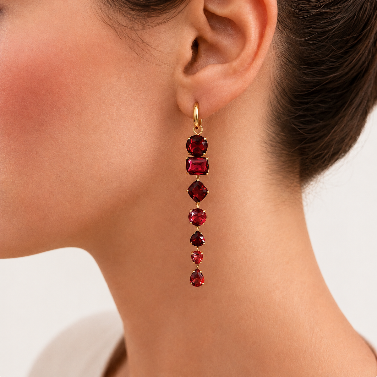 Dominique garnet drop earring worn on a model, with a long line of deep red gemstones suspended from a small gold hoop.