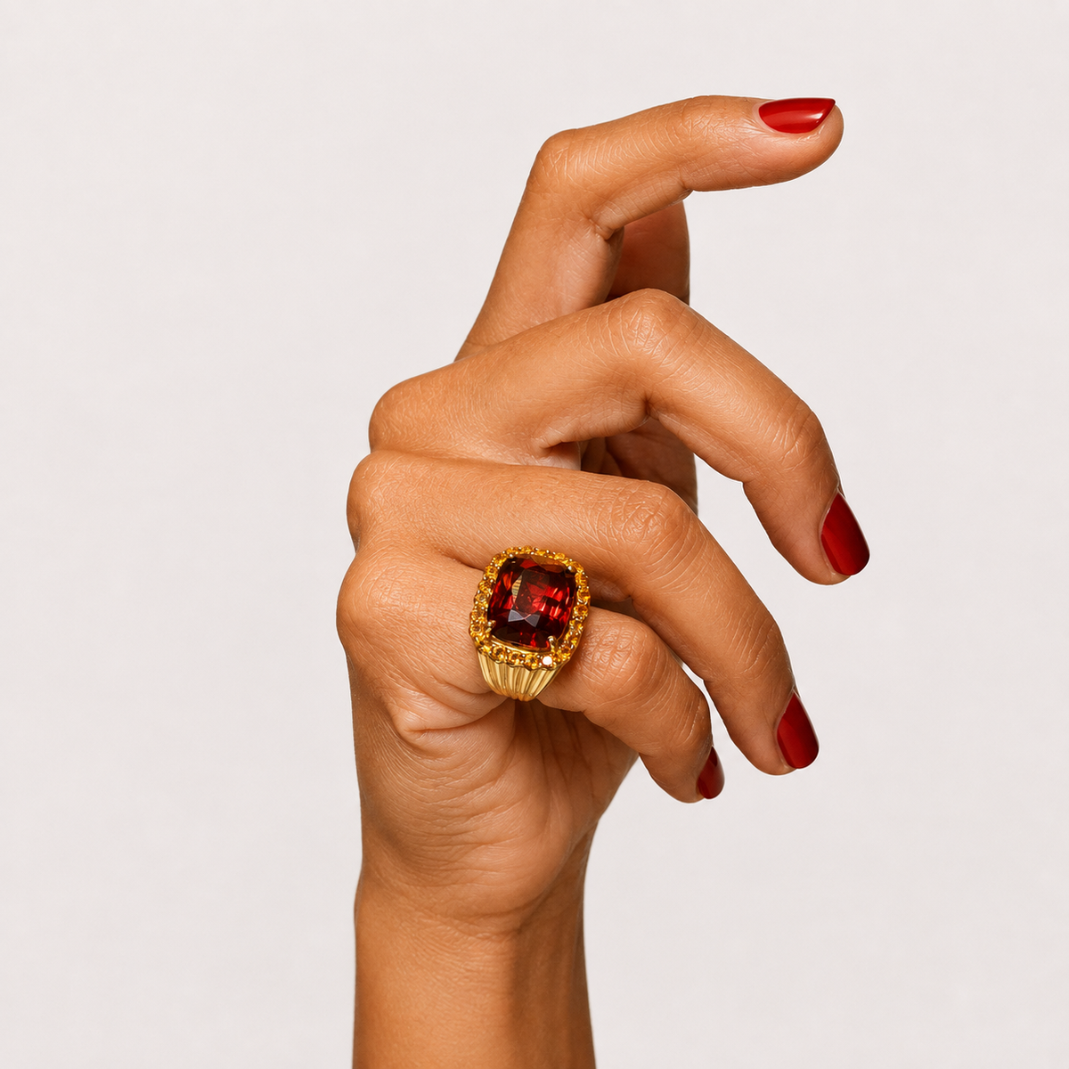 Raj 18K yellow gold ring worn on a hand, with a deep red garnet centre and a halo of golden citrine.