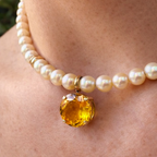 Round golden citrine charm in an 18K gold claw setting, worn on a short white pearl necklace.