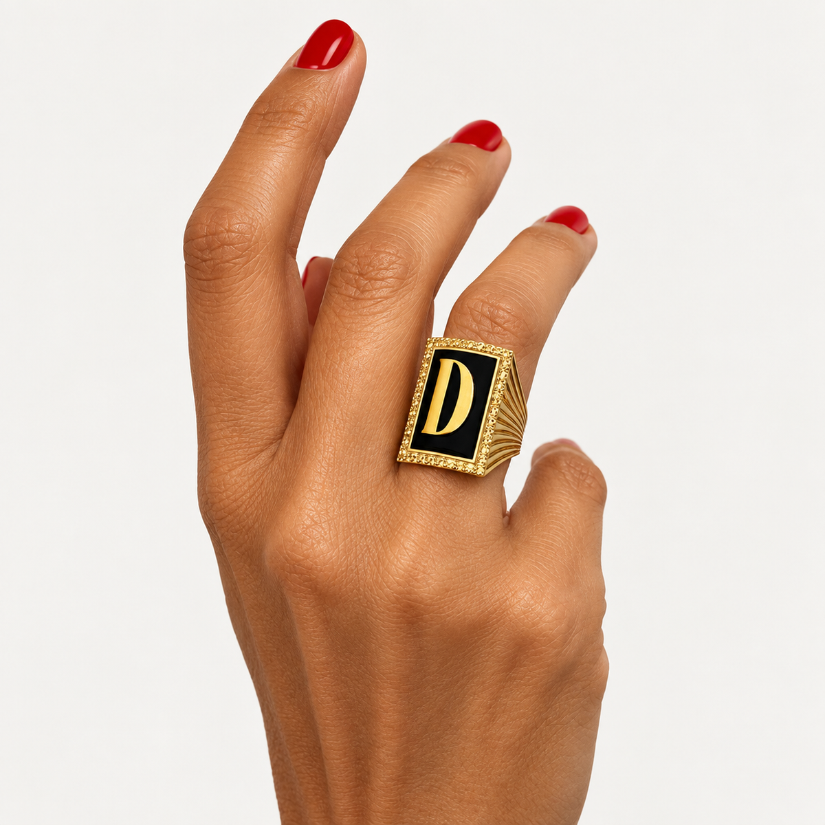 18K gold initial D ring with black onyx and a golden sapphire halo, worn on a hand with red nails.
