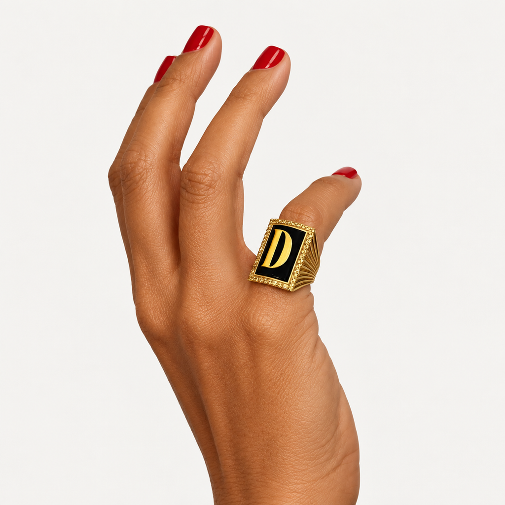 Initial D ring in 18K gold with black onyx, shown from an angle on a hand with red nails.