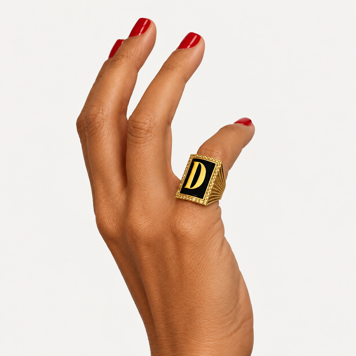 Initial D ring in 18K gold with black onyx, shown from an angle on a hand with red nails.
