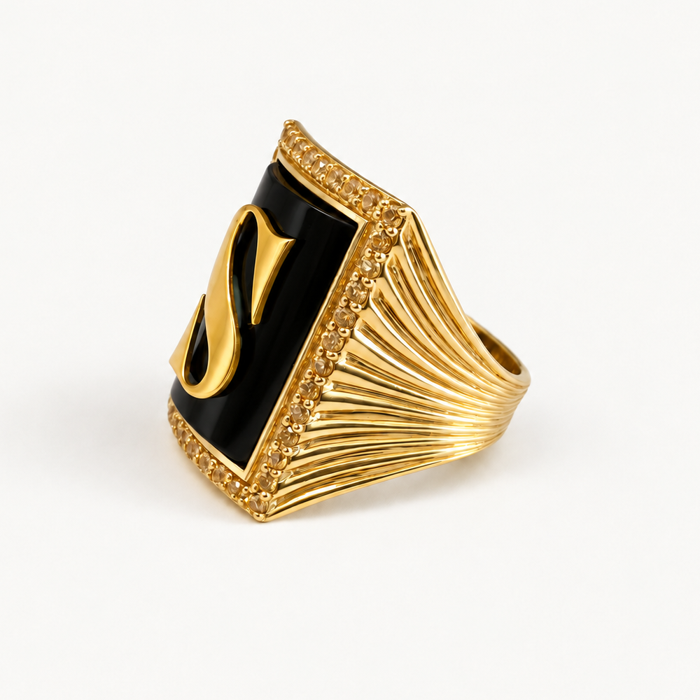 Angled view of the 18K gold initial S ring showing black onyx, a golden sapphire halo and a fluted band.