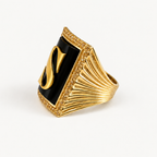Angled view of the 18K gold initial S ring showing black onyx, a golden sapphire halo and a fluted band.