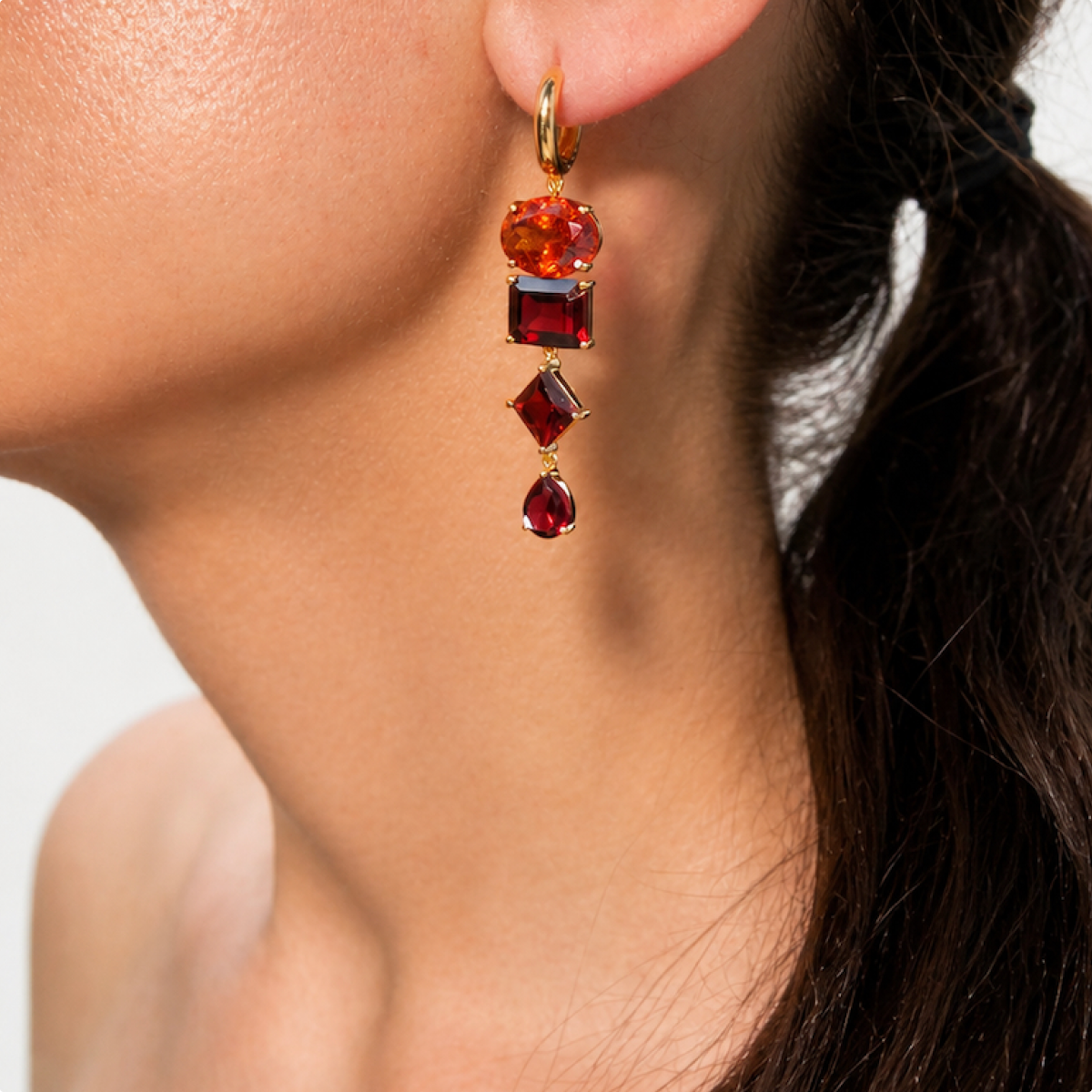 Nathalie garnet earring worn at the ear, with oval, square, diamond-shaped and pear-shaped stones hanging from a small gold hoop.