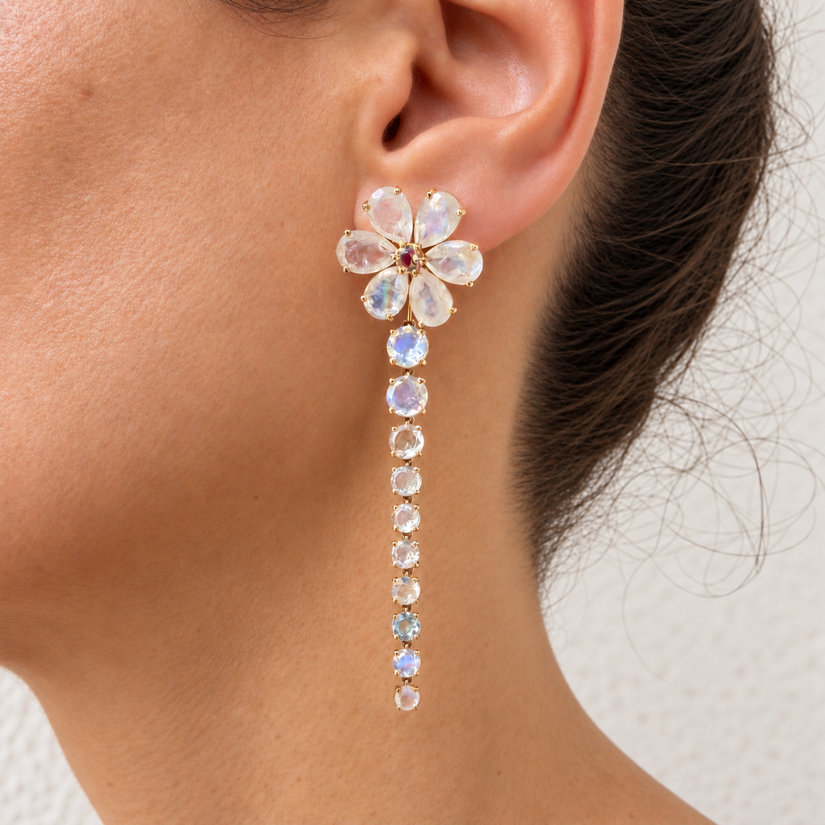Nayla rainbow moonstone earring worn on a model, with a flower at the ear and a long line of round stones in gold.