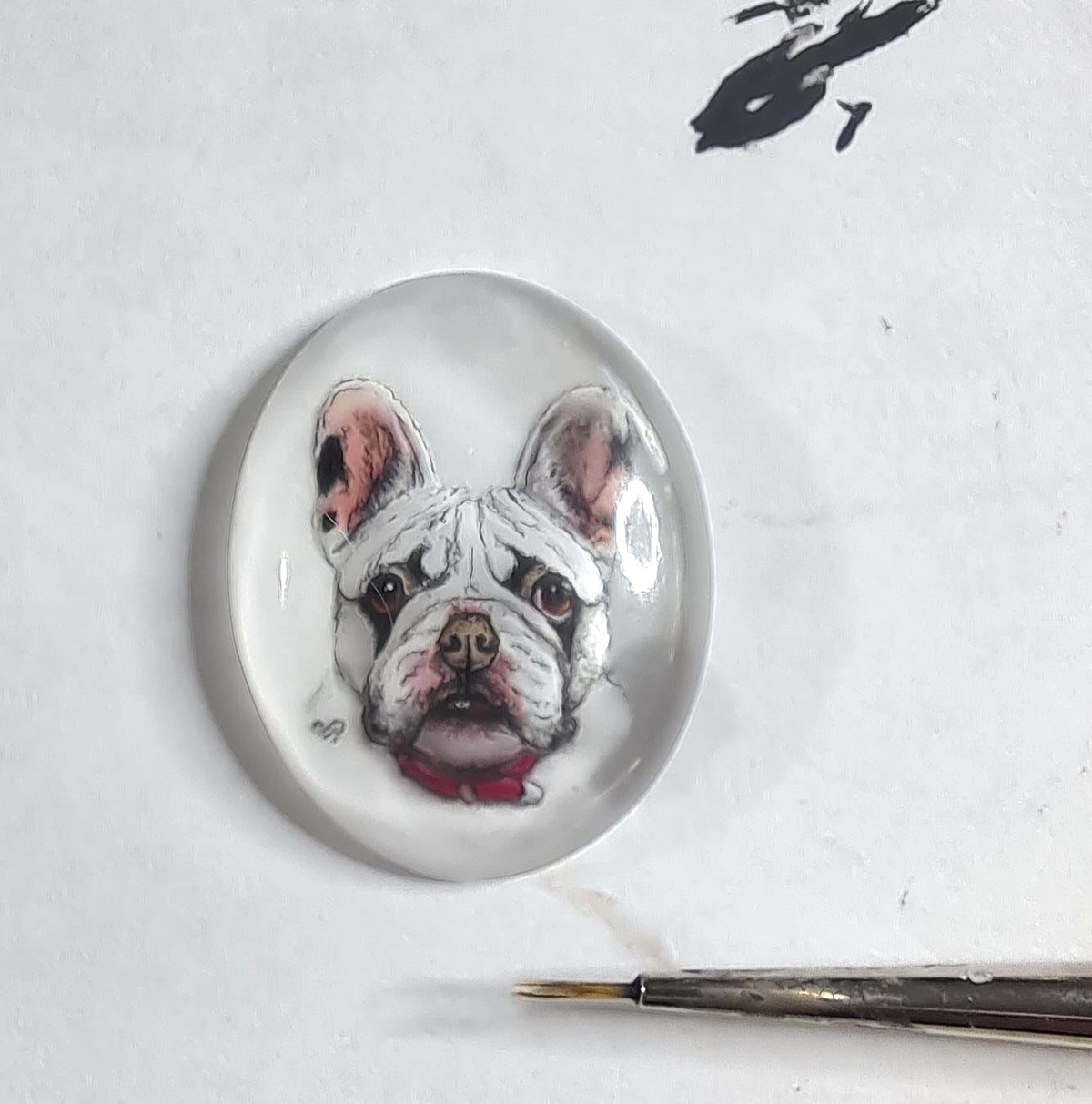 Hand-painted French bulldog portrait in an unset oval rock crystal beside a fine paintbrush.