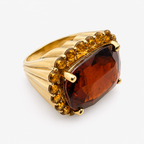 Angled close-up of the Raj garnet and citrine ring, showing the faceted red centre stone and fluted gold shoulder.