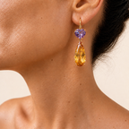 Roubini earring worn at the ear, showing a purple amethyst heart above a long golden citrine teardrop on a small gold hoop.