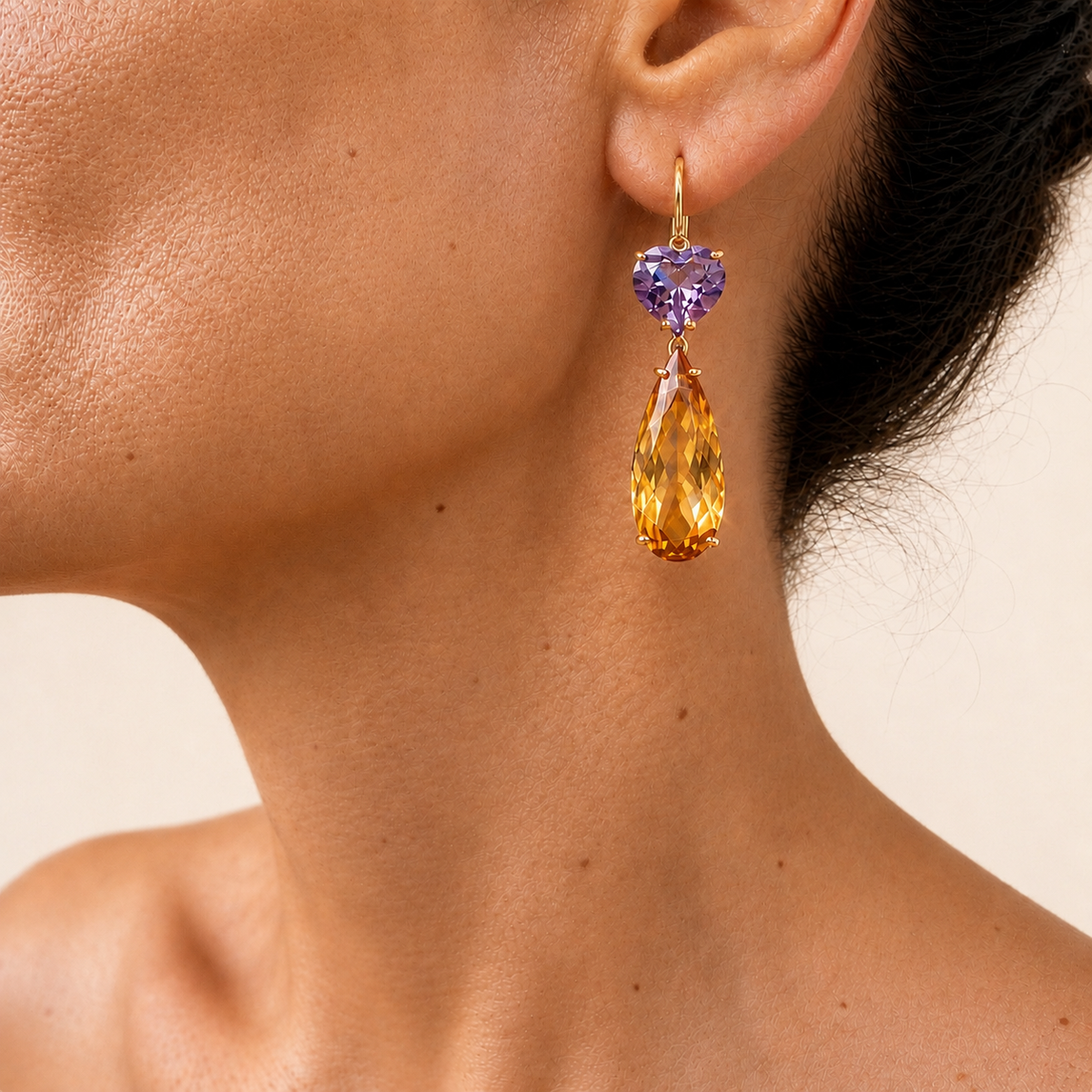 Roubini earring worn at the ear, showing a purple amethyst heart above a long golden citrine teardrop on a small gold hoop.