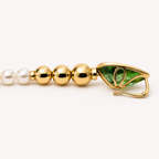 Side view of the Salwa peridot snake-head clasp, showing its open hinged fastening beside graduated gold beads and pearls.