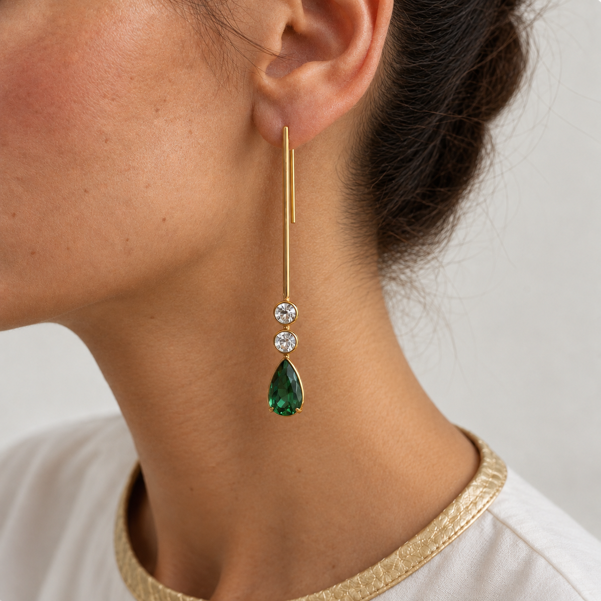 Serena 18K gold stick earring worn on the ear, with two round aquamarines and a pear-shaped green emerald drop.