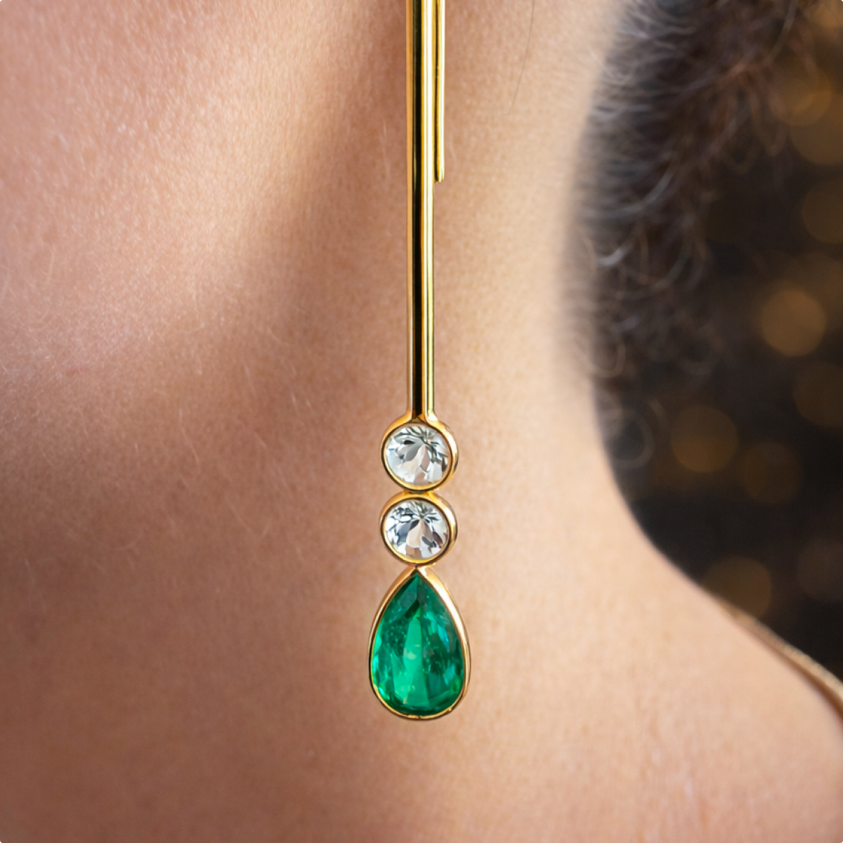 Close-up of the Serena earring worn at the ear, showing two aquamarines above a pear-shaped emerald in gold bezel settings.