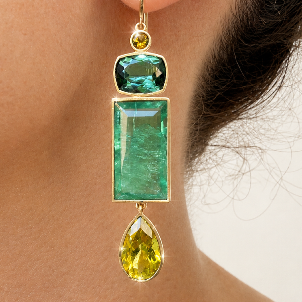 Close-up of the Souraya earring worn at the ear, showing dark green tourmaline, rectangular fluorite and an olive tourmaline teardrop in gold.