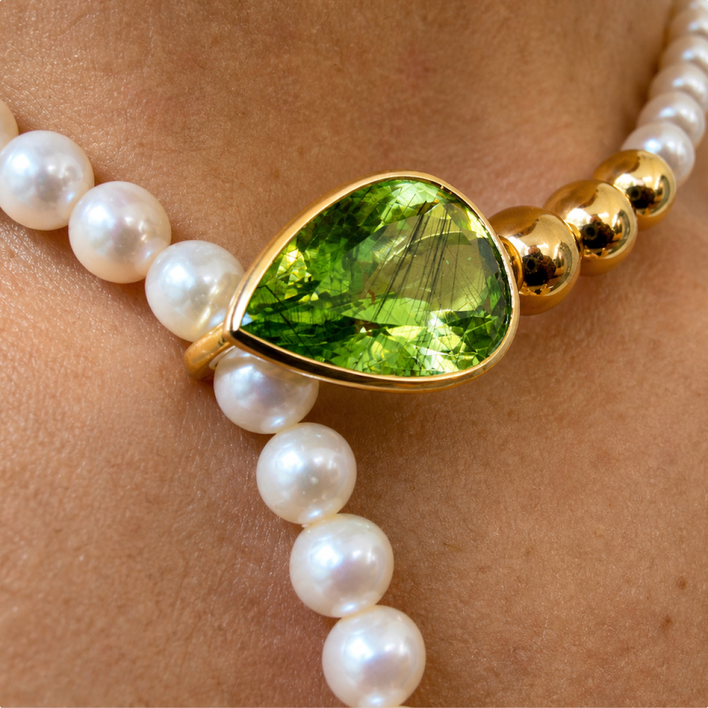Close-up of the Salwa necklace worn at the neck, showing the pear-shaped peridot clasp between white pearls and polished gold beads.