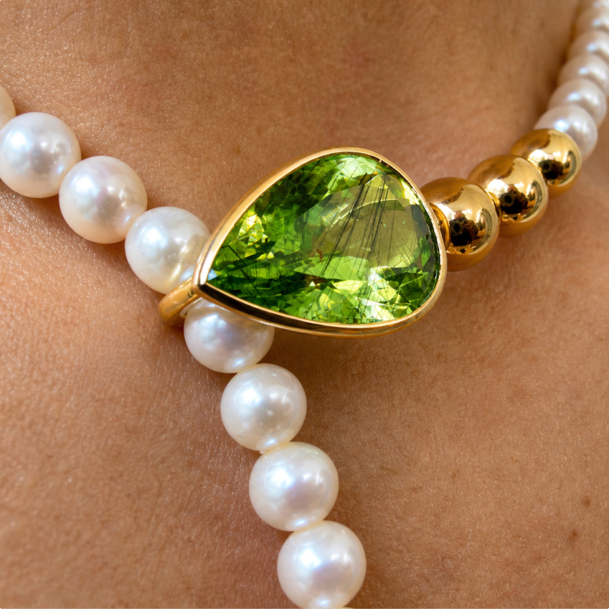Close-up of the Salwa necklace worn at the neck, showing the pear-shaped peridot clasp between white pearls and polished gold beads.